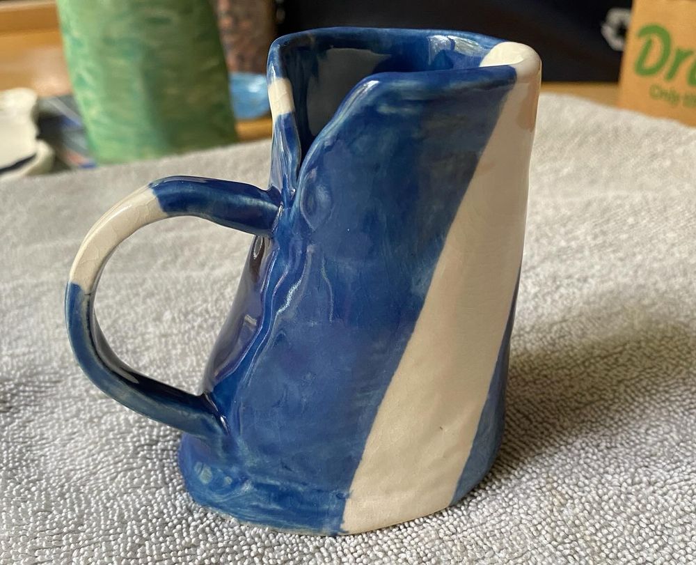 A small blue pitcher with white thick stripes on the side and handle and an off-set handle 