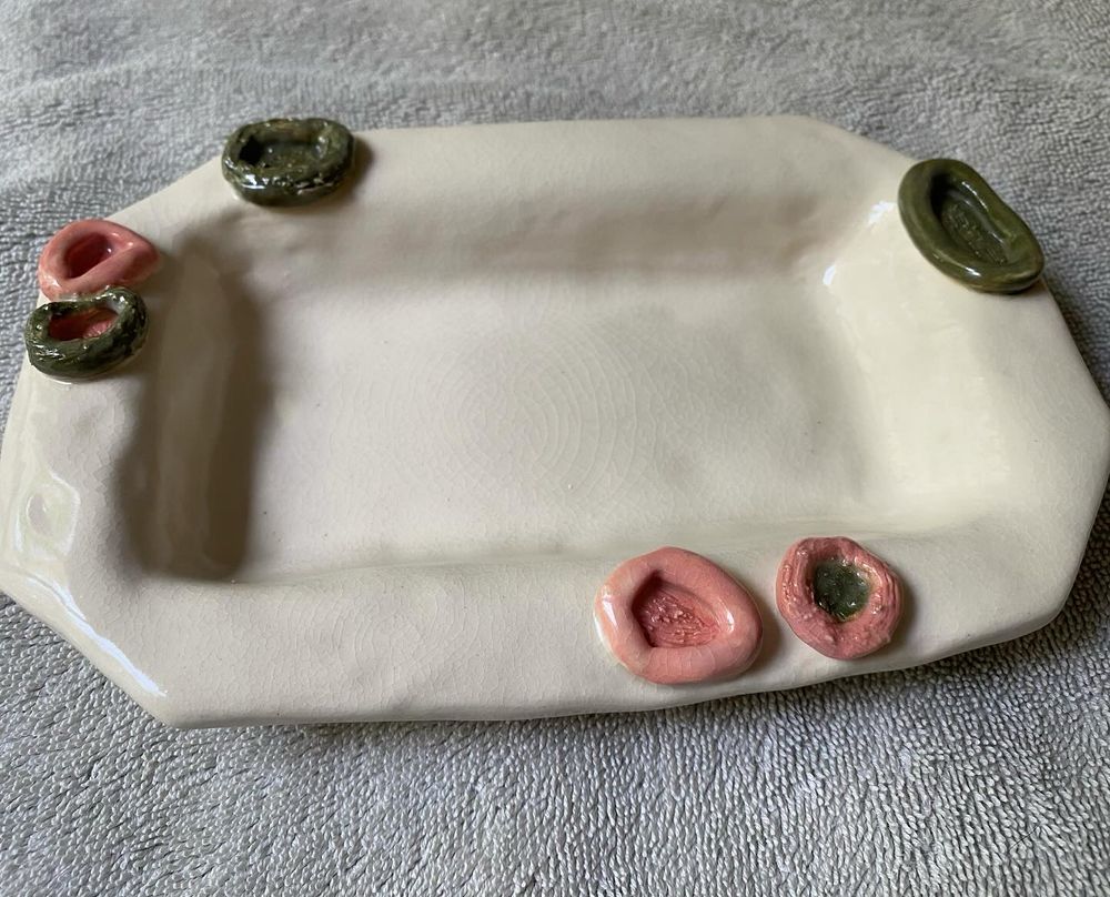 A cream colored rectangle ceramic dish with green and pink raised circles scattered on the rim