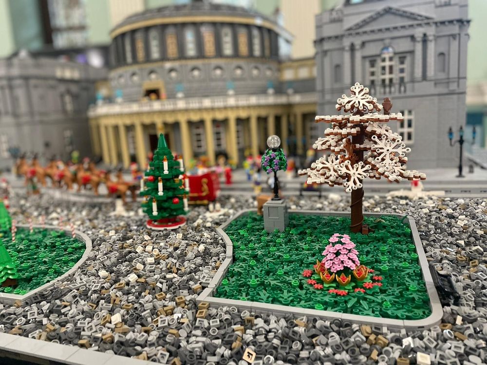A festive LEGO display depicting the National Library of Ireland adorned with Christmas decorations. The intricate model features LEGO Christmas trees, vibrant festive scenes with mini LEGO people enjoying the holiday spirit, and a charming Santa Claus figure with his LEGO reindeer poised as if ready to take off. The iconic architecture of the library is beautifully rendered in LEGO bricks.