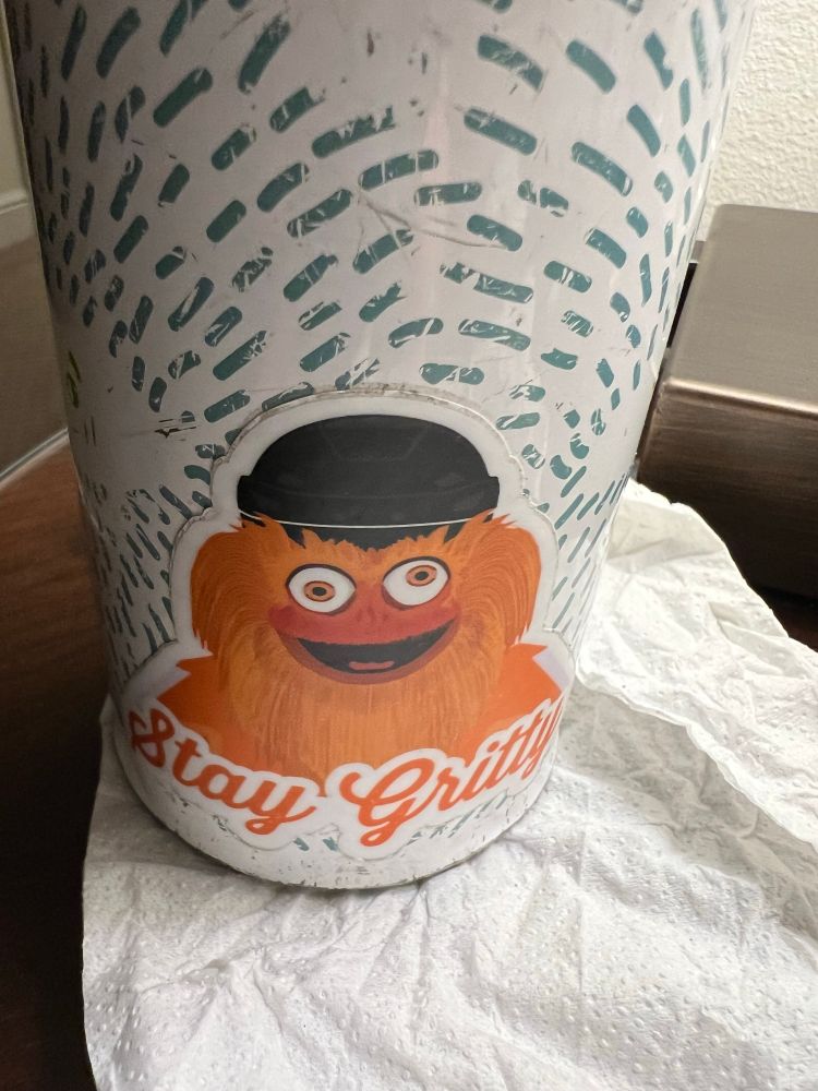 A sticker showing the fluffy orange mascot known as Gritty, stuck to a white water bottle decorated with green dashes.