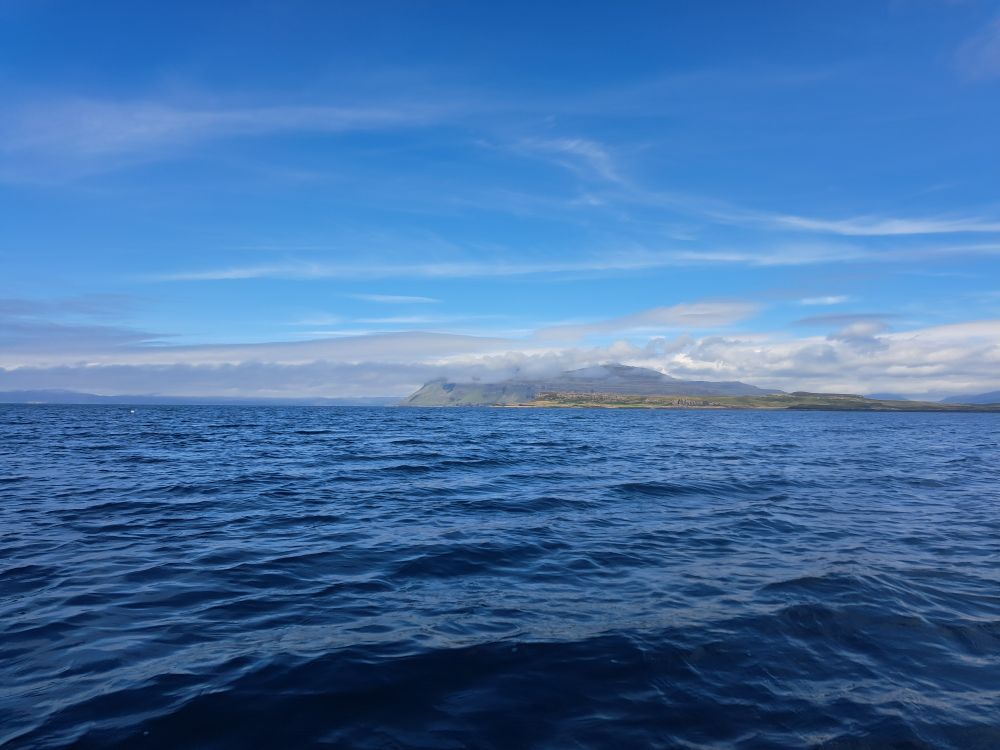 Blue sea and sky, a volcanic mountain shrouded in clouds.
