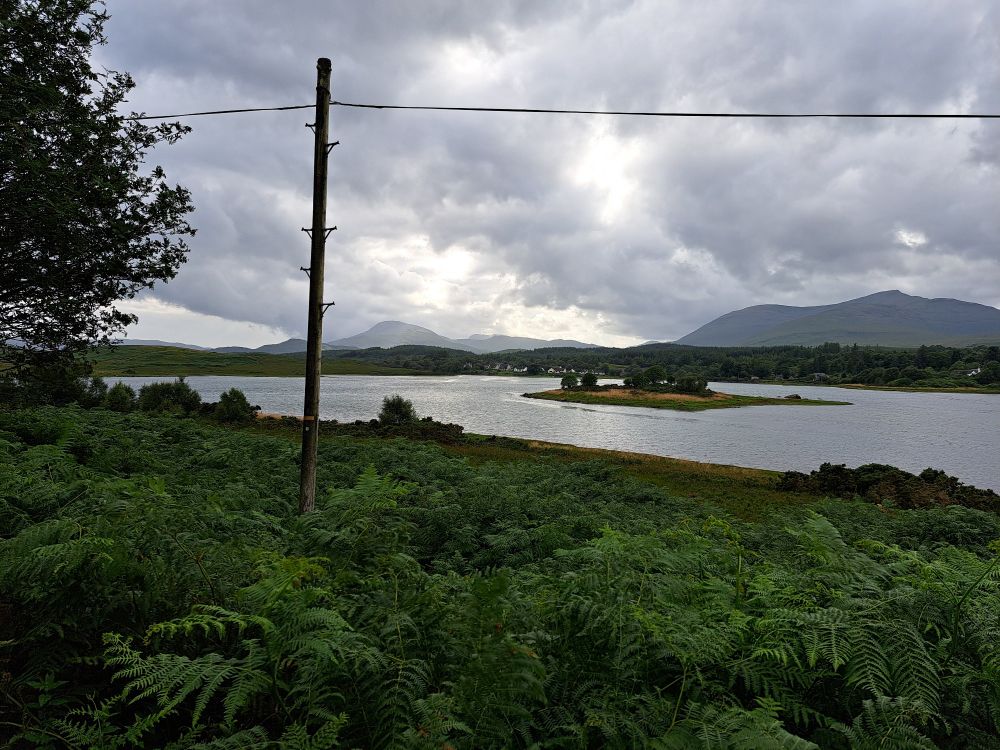 A grey cloudy sky, green bracken, mountains and loch don 