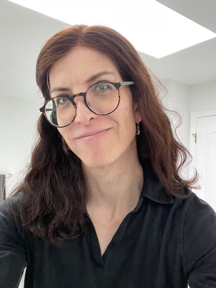 Rook in a casual black shirt, hair pinned away from her face, smiling in a white room