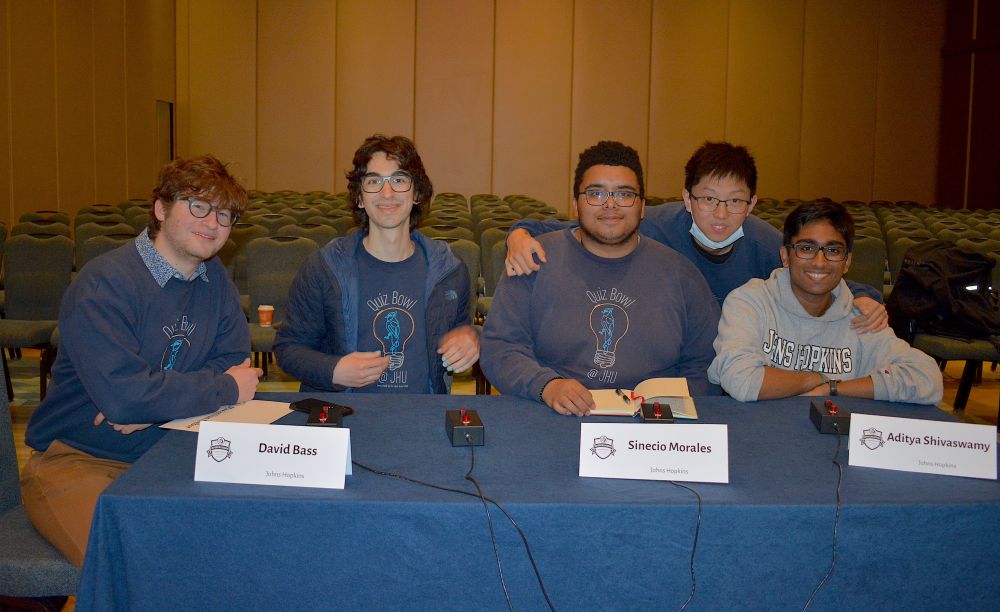 Group photo of the Johns Hopkins University quizbowl team, shortly before round 1 of NAQT's 2025 Intercollegiate Championship Tournament. We are (mostly) wearing matching navy team sweaters. We sit in a large hotel convention space.