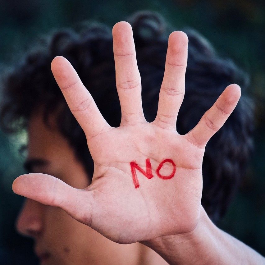 Person with their open hand raised and spread in front of them. The word "no" is written in red on their palm.