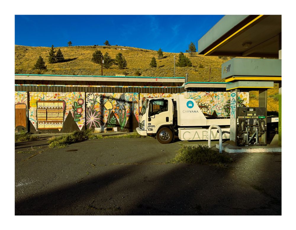 Photo of a carvana truck at an abandoned gas station 