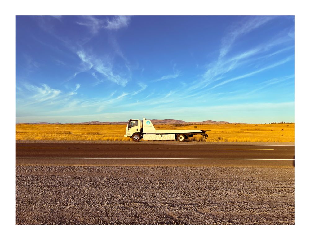 Photo of a carvana truck on a scenic road through the desert 