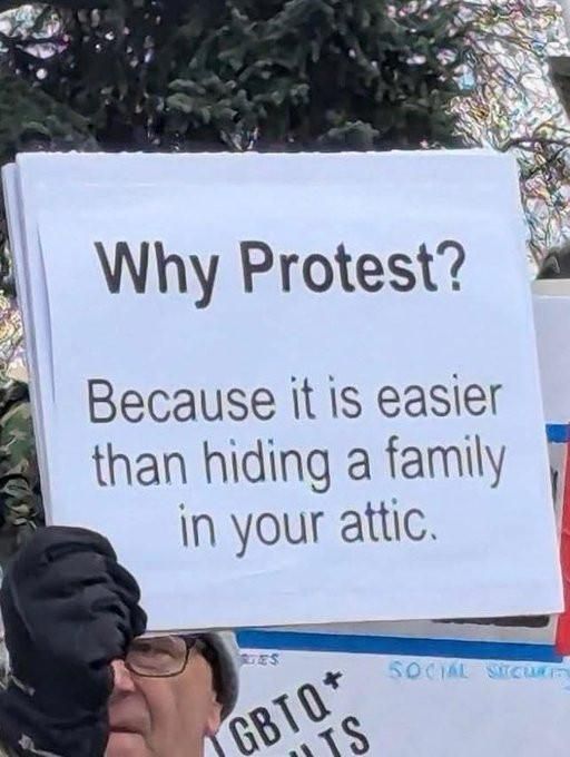 Someone hold’s up a sign:
Why Protest? 
Because it is easier
than hiding a family 
in your attic.
