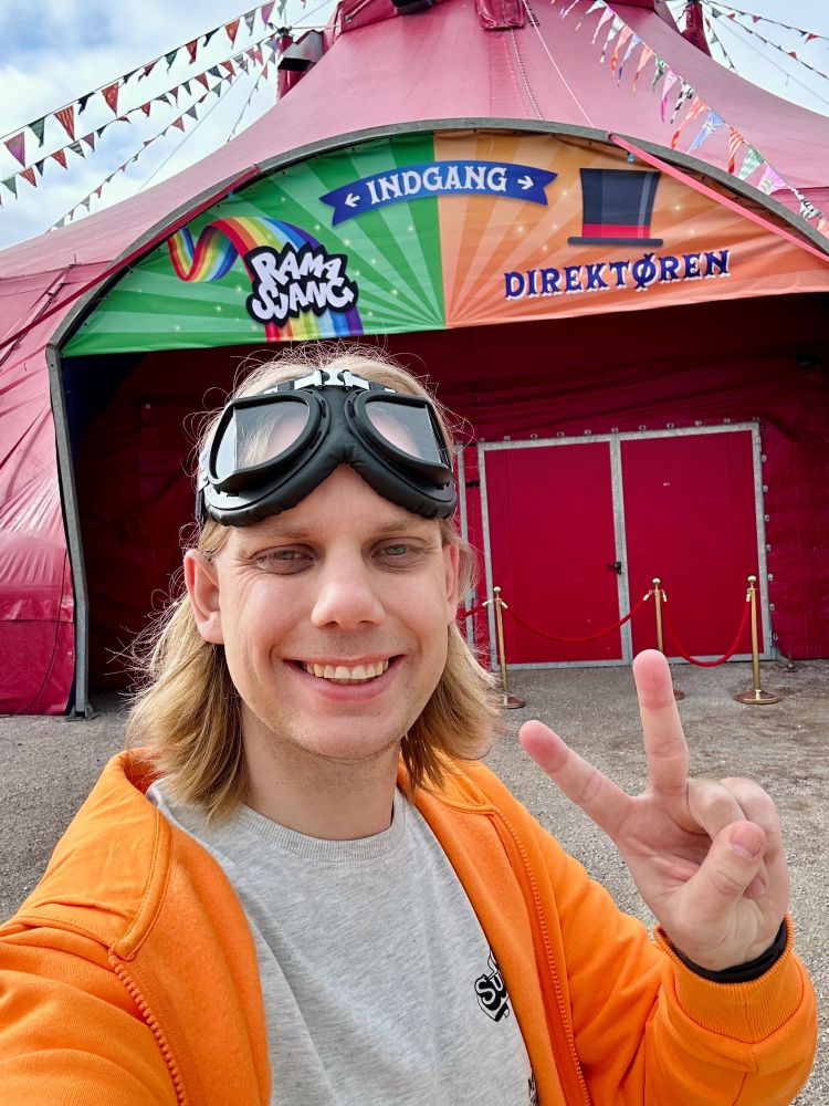 Me wearing t-shirt and hoodie branded with the circus’ logos in front of the big circus tent.