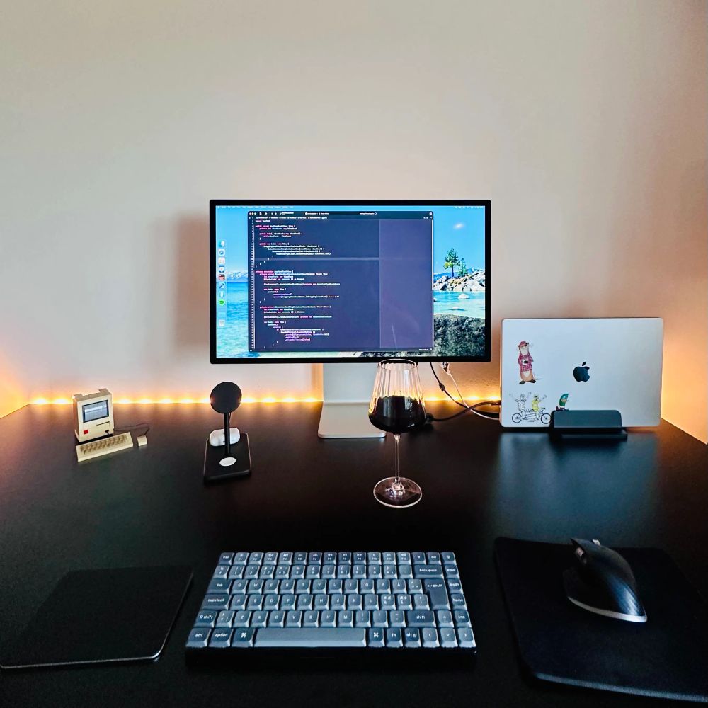 My desktop with a Studio Display and a MacBook Pro. Running Xcode. In front of the display is a glass of red wine. On the desk is also a trackpad, a keyboard, and a mouse along with some LEGO.