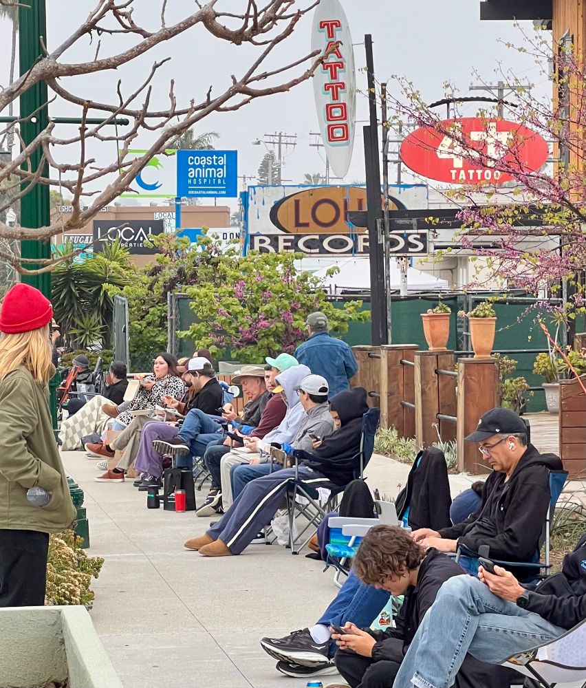 A street scene with a bunch of people in line, sitting in chairs and spread out blankets waiting to get into Lou’s Records in Encinitas 