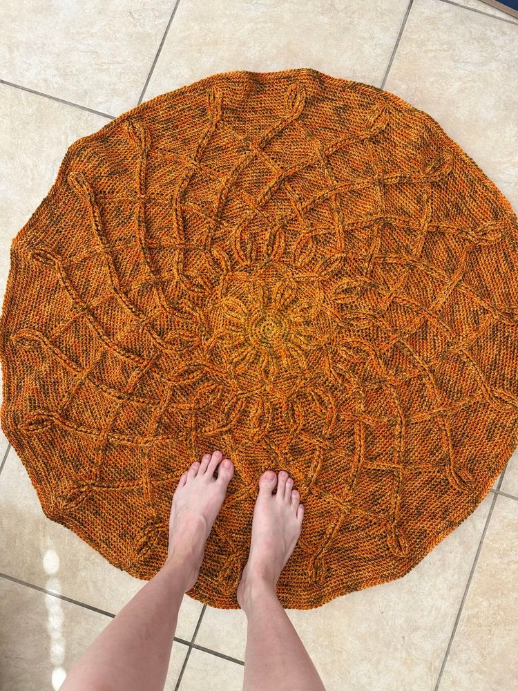 My feet standing on a round orange crochet rug on beige tile floor