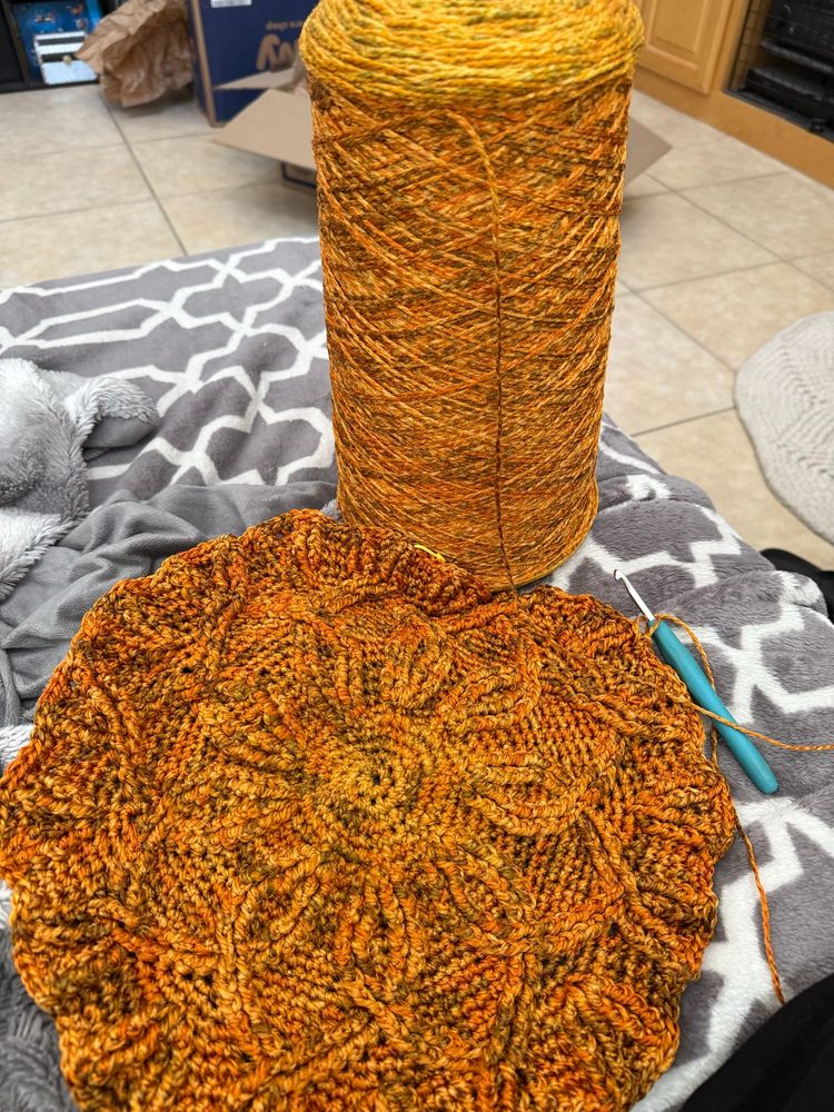 Orange cone of yarn next to the beginning round piece of densely crocheted rug.