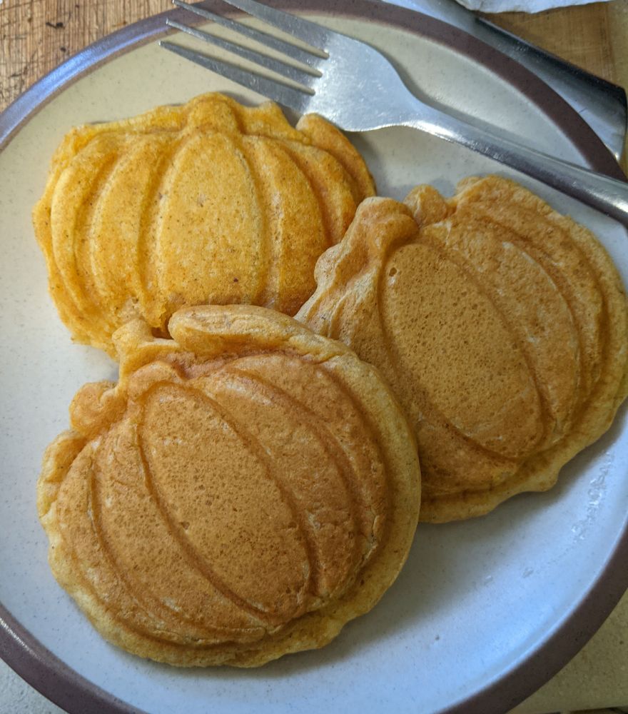 three orange-colored waffles in the shape of pumpkins on a plate with a fork