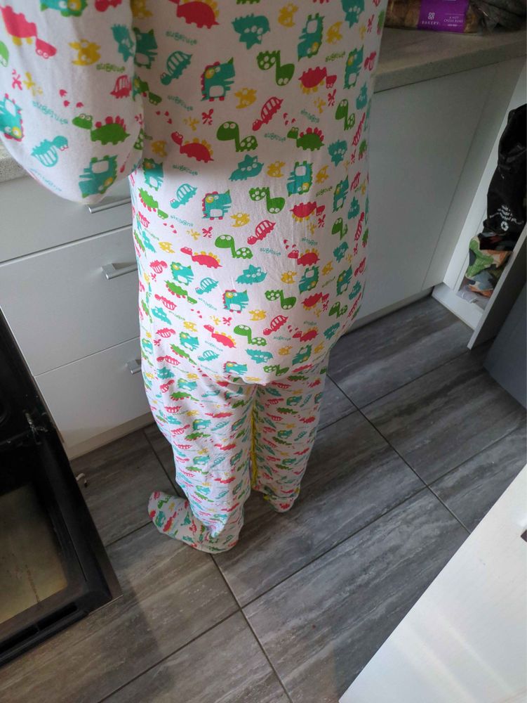 Padded boy cooks dinner in Dino footed sleeper