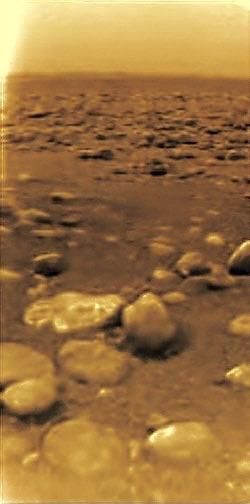 The surface of Saturn's moon Titan, an eerily yellow, desert-like landscape covered with rocks 
