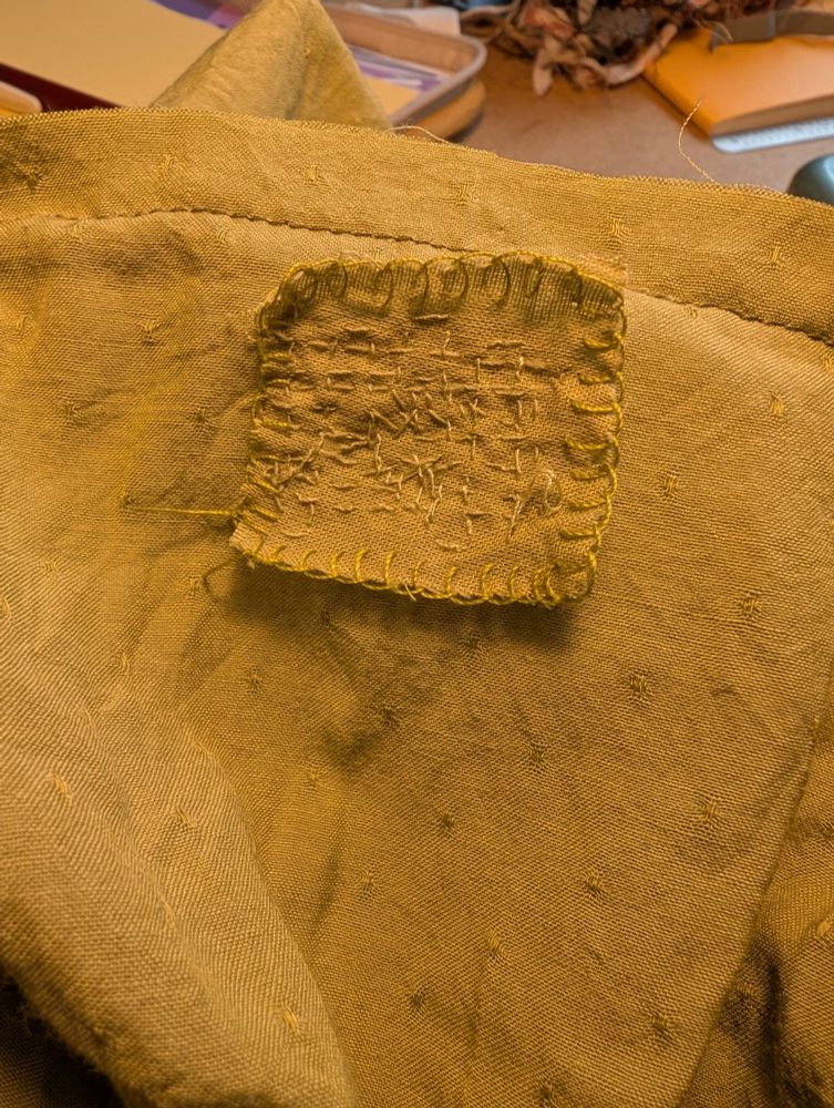 The patch on the inside of a mended chartreuse colored skirt, with messy teeny stitches in the middle and the edges of the patch finished with a blanket stitch