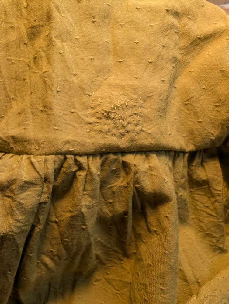 A mended tear in the body of a chartreuse skirt with very small, messy stitches