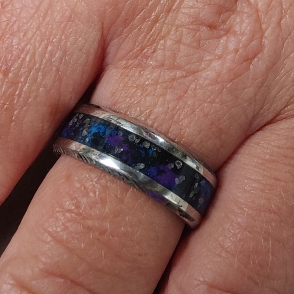 Ein silberner Ring mit dunkelblaulila leuchtender Einlage in der Mitte mit glitzernden Punkten 