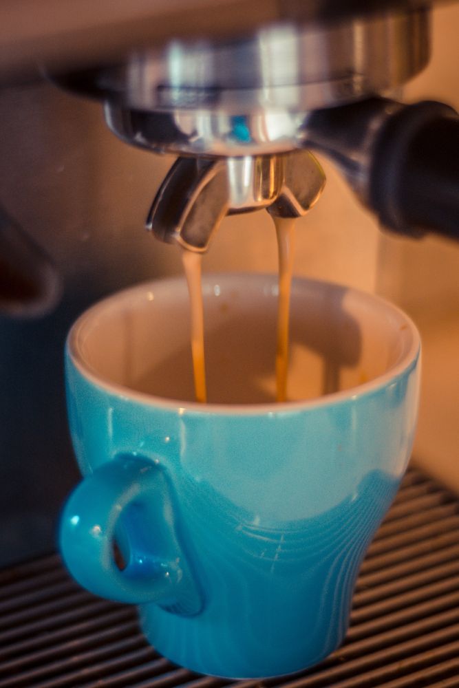 An espresso shot pouring into a tulip shaped light blue coffee cup