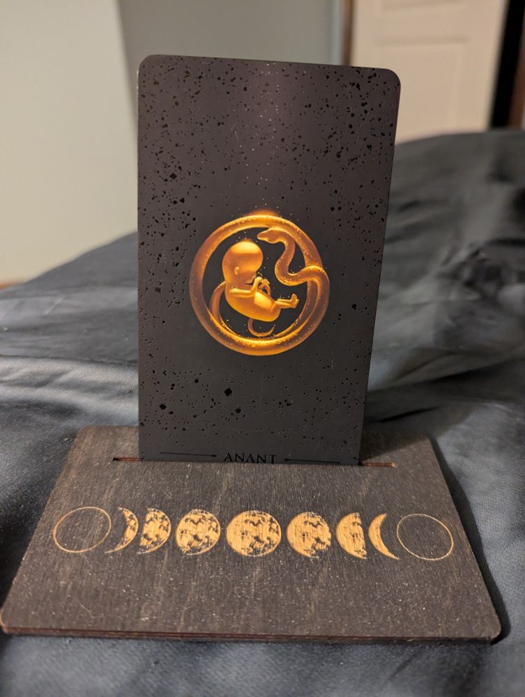 Anant, a special card only for the True Black deck. A golden baby fetus floats on a speckled black card. The baby's umbilical cord loops around it in a circle, ending in the head of a snake. 