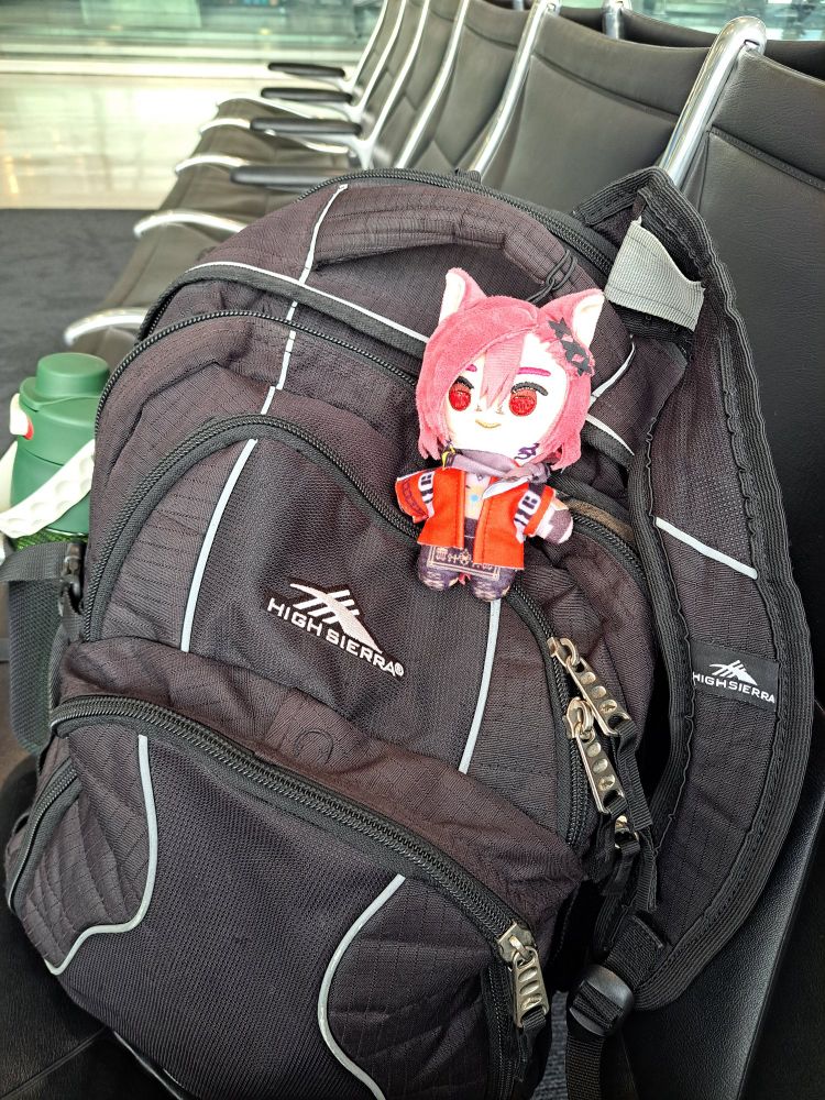 A black backpack on a seat, a G'raha Tia plush is on top of it.