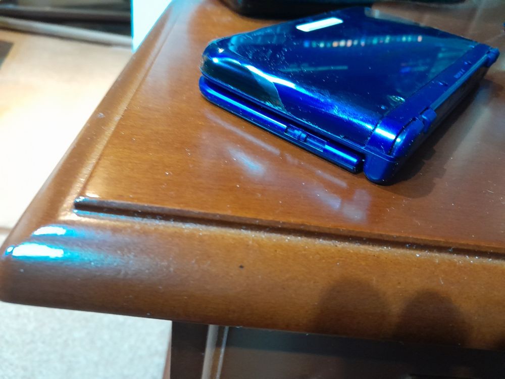 Blue New Nintendo 3DS XL with paint missing on a corner on a wooden desk.