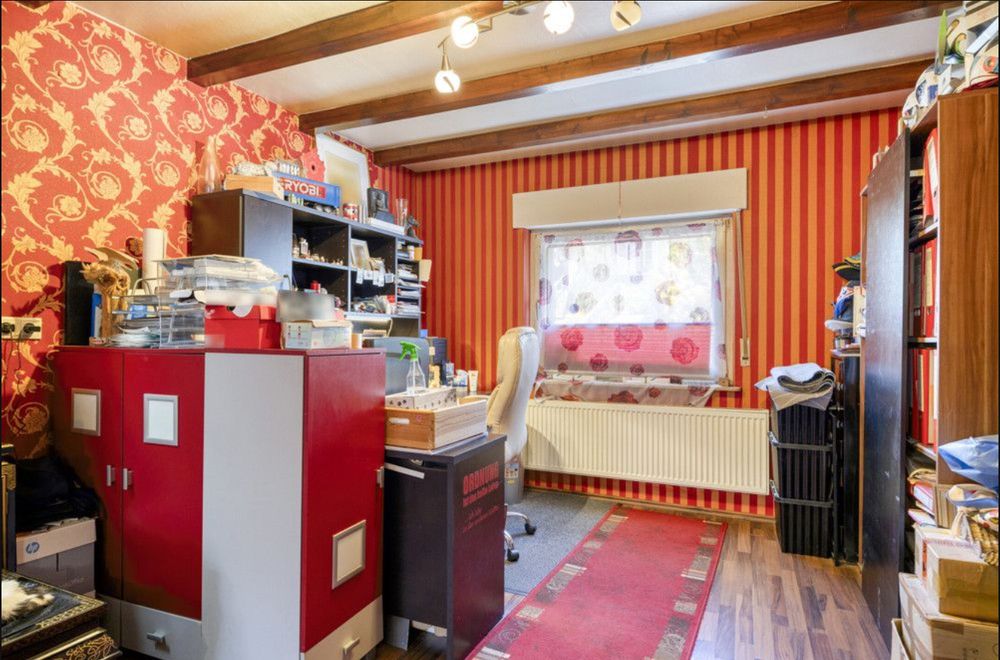 a somewhat cluttered office with red wallpaper, carpet and furniture