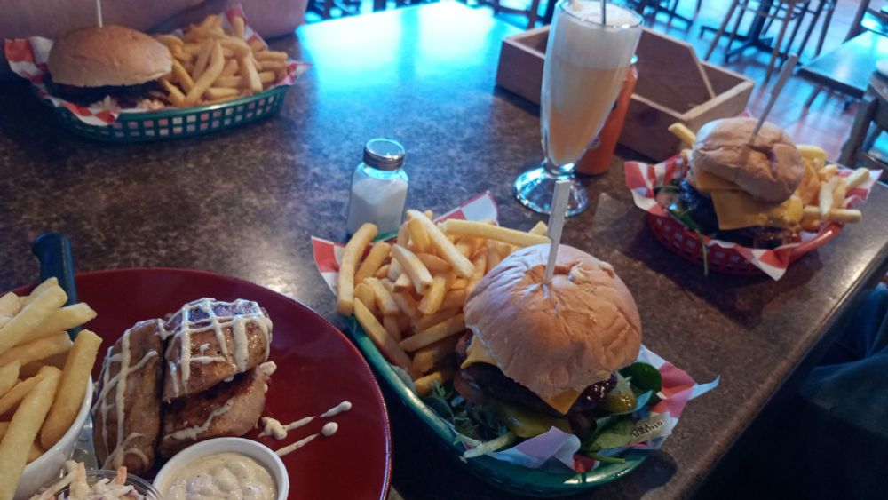 A booth table at a BBQ joint. There are 3 burgers, all with a serving of hot chips. Or fries. There's also an ice cream float, but we Aussies call them spiders.


There's also a plate of cajun chicken. Also with chips, and coleslaw. Who is eating all that... 