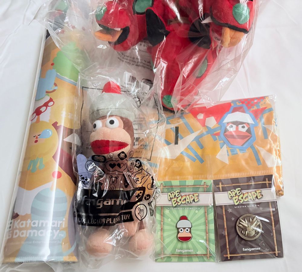 Fangamer merchandise: stuffed pipo monkey, pipo monkey pin, specter coin pin, pipo shirt, Katamari desk mat, hades Cerberus plush