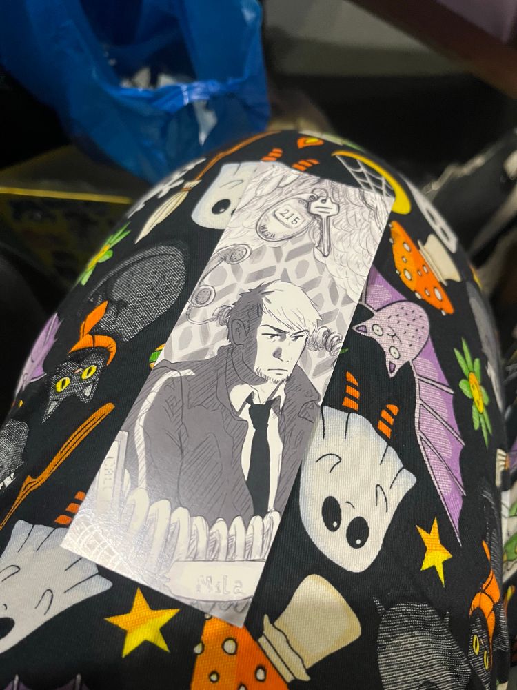 Image of a bookmark laying on a Halloween pants leg with a black and white image of a white male and a hotel key with 215 on the keychain 