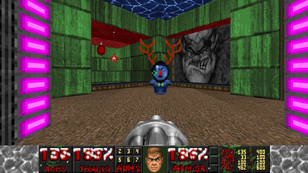 Blue Armor with a green bow tie, and a mega health sphere with reindeer antlers and a red nose sits in the center of a room with green walls and a brown floor. To the right is a large wall with an evil looking elf chiseled within.