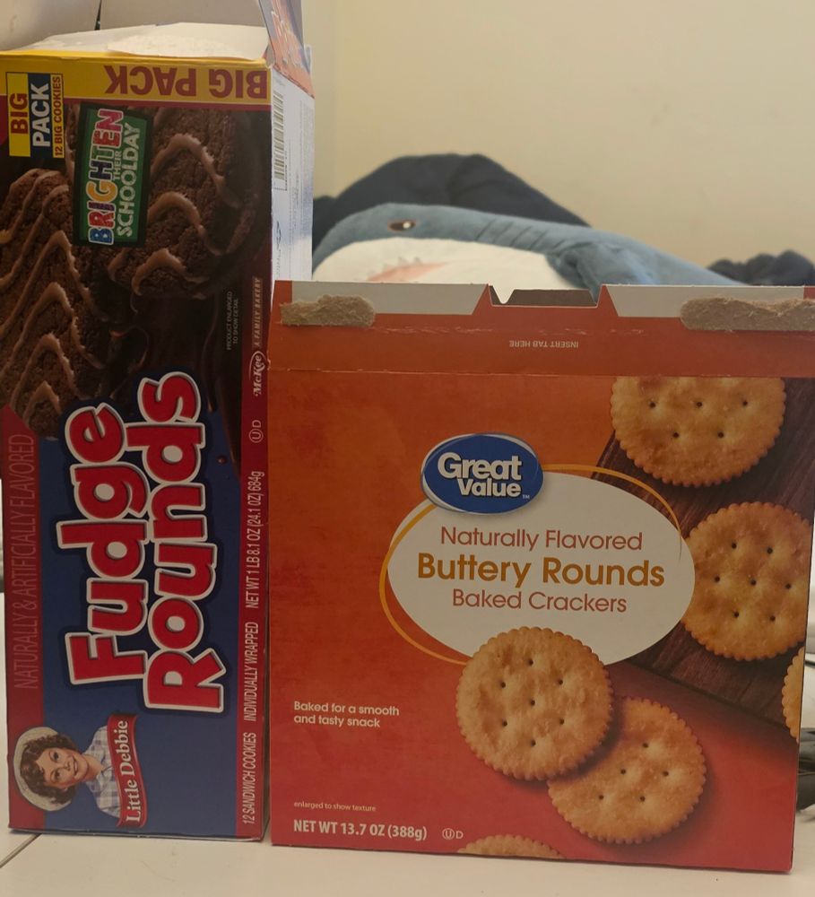 A box of 'fudge rounds' and a box of 'buttery rounds baked crackers' with a sneaky Blåhaj in the background.
