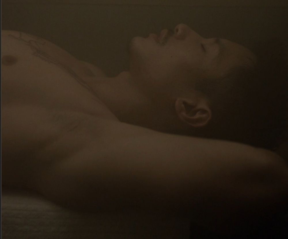 Manny jacinto profile lying down in a sauna, shirtless and eyes closes, swathed in steam 