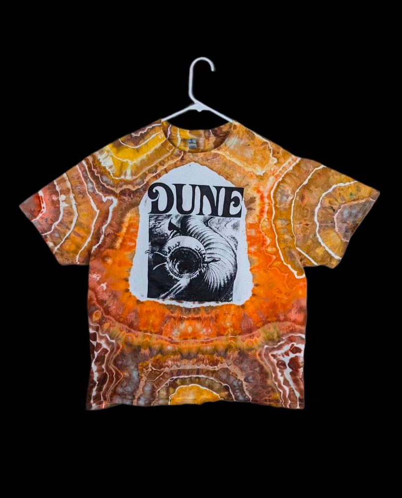 A graphic t-shirt with the text "DUNE" and a picture of a sandworm.  Around the graphic, I have left blank space and then dyed the rest of the shirt brown, yellow, and orange in a pattern reminiscent of geodes or a topographic map.  