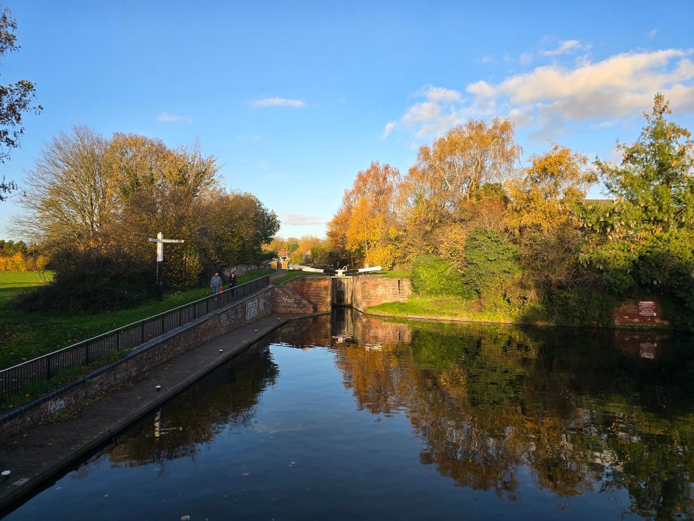 Canal junction.A picturesque canal on a sunny autumn day. The water reflects the colorful yellow and green trees lining the banks and the bright blue sky above. A stone bridge and lock gates are visible in the distance