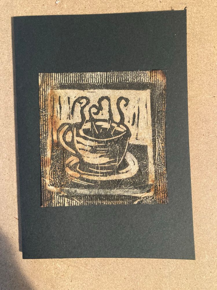 A small Lino print featuring a teacup with steaming tea printed onto a used teabag