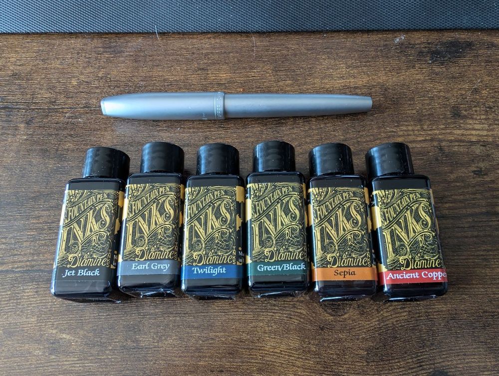 a row of fountain pen ink bottles of varying colours and a silver Sheaffer pen
