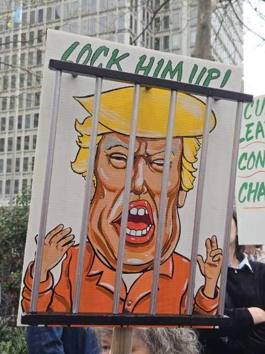 Cartoon drawing of Trump looking furious behind bars and wearing orange with the words Lock Him Up!