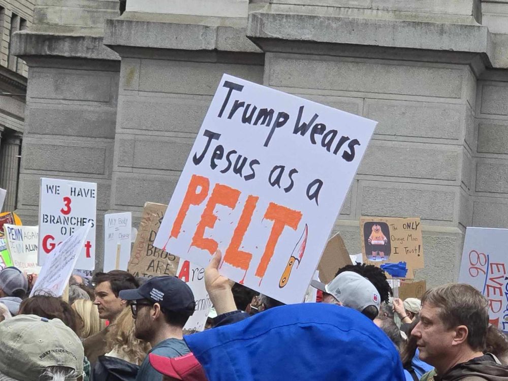 A protest sign reading Trump Wears Jesus As a Pelt