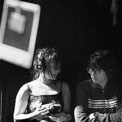 Black and white photo of two Chinese women wearing wireless headphones. One holds a Polaroid camera.
