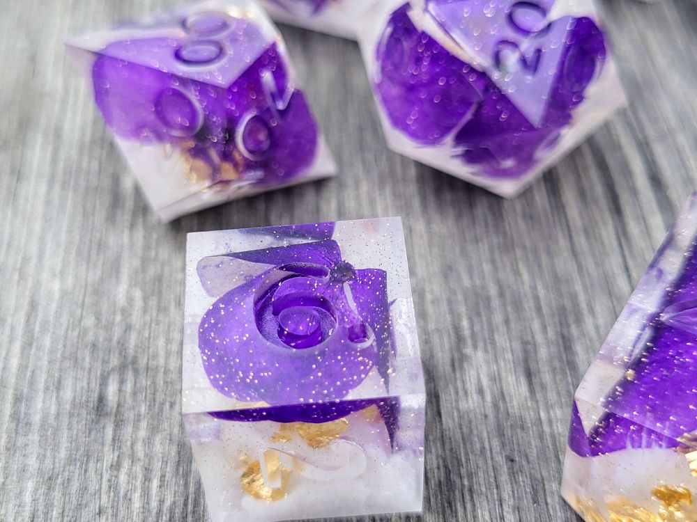 7 piece handmade dice set with dehydrated purple pansies, white ink & gold leaf inside; dice set is "raw" (unpolished & uninked) in photo