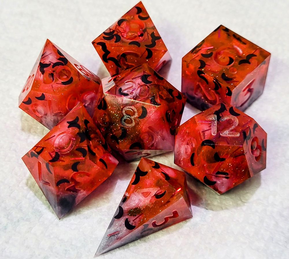 pictured is a handmade, unpainted 7 piece polyhedral dice set made with red, black, & white alcohol inks and inclusions of black cresent Moons & red micro tinsel 