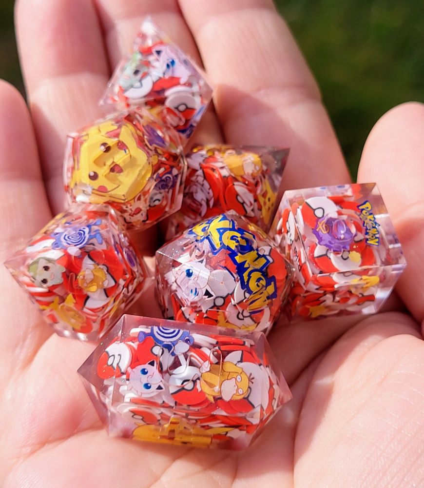 pictured is a handmade 7 piece polyhedral dice set that is done in a Pokémon theme; the interior of the dice are filled with red & white pokeballs & decals of various Pokémon 
