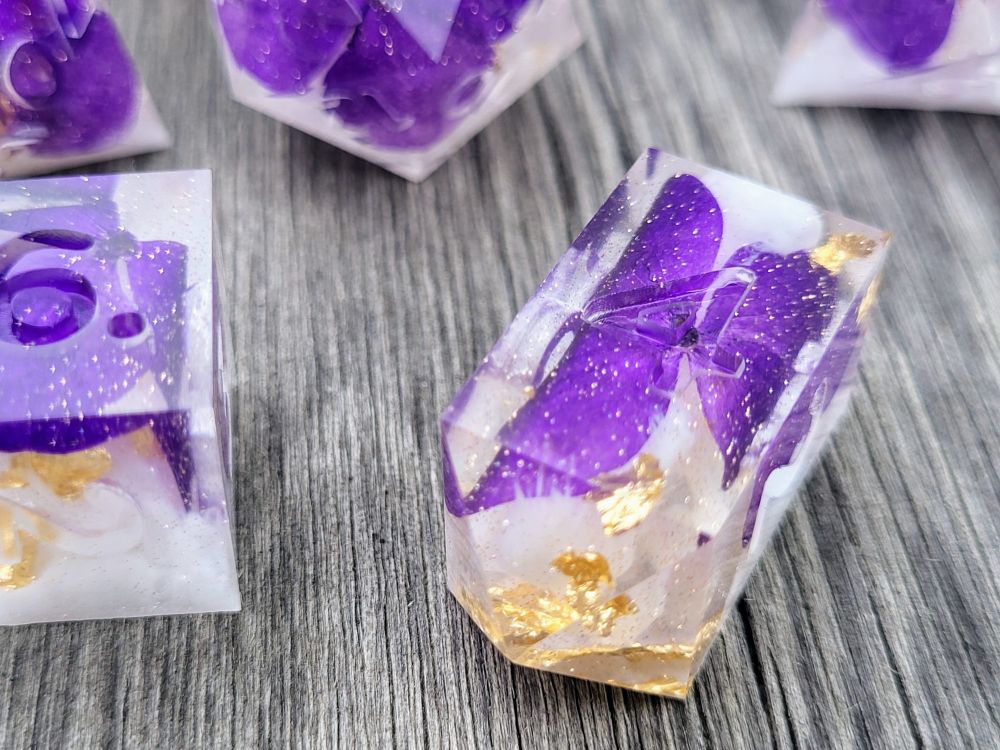7 piece handmade dice set with dehydrated purple pansies, white ink & gold leaf inside; dice set is "raw" (unpolished & uninked) in photo