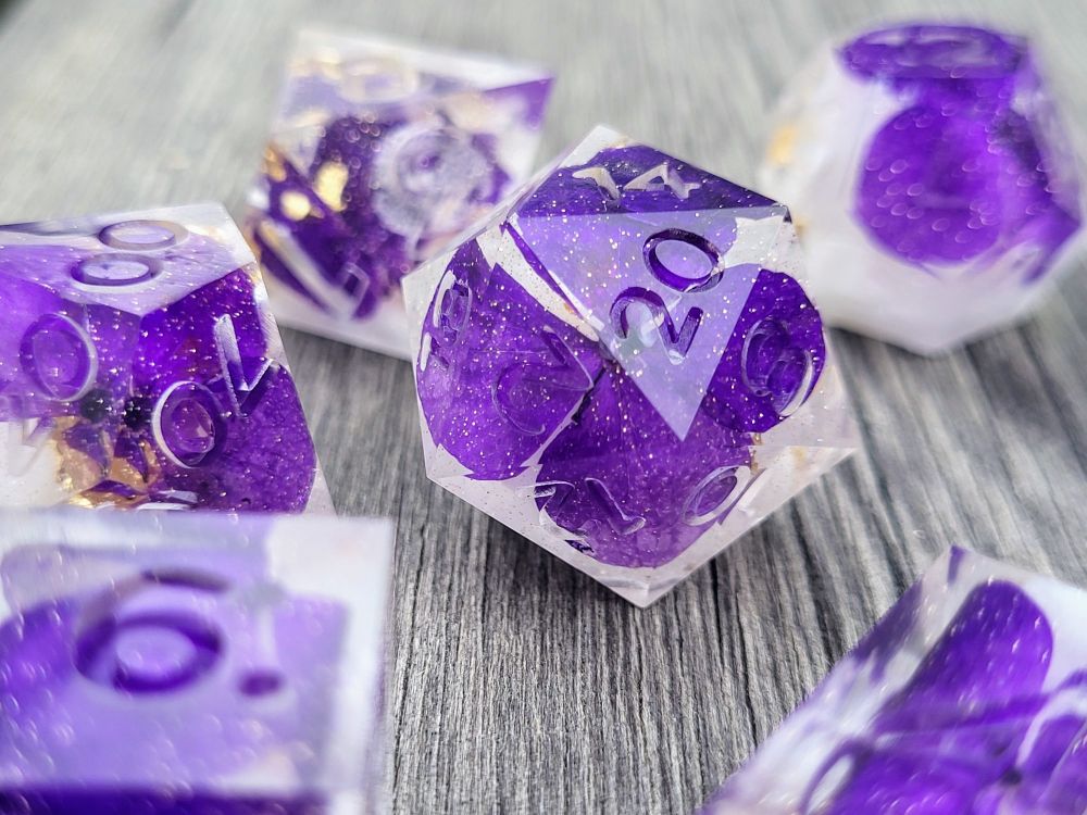 7 piece handmade dice set with dehydrated purple pansies, white ink & gold leaf inside; dice set is "raw" (unpolished & uninked) in photo