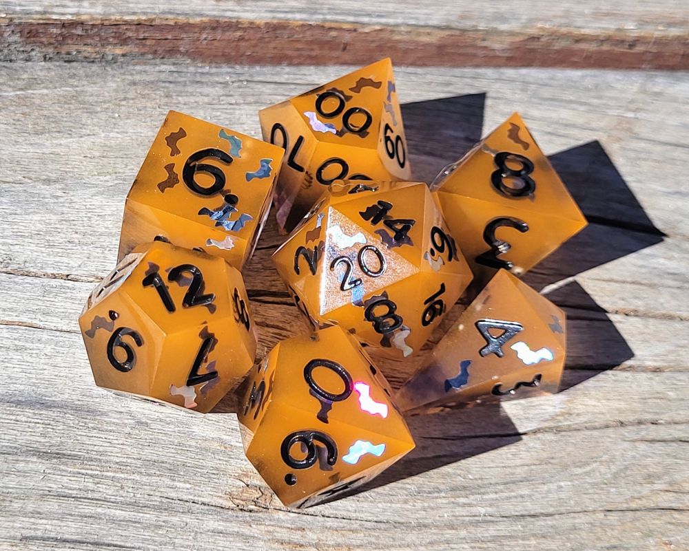 pictured is a handmade 7 piece polyhedral dice set in orange & black with holographic black bat glitter randomly placed in each die