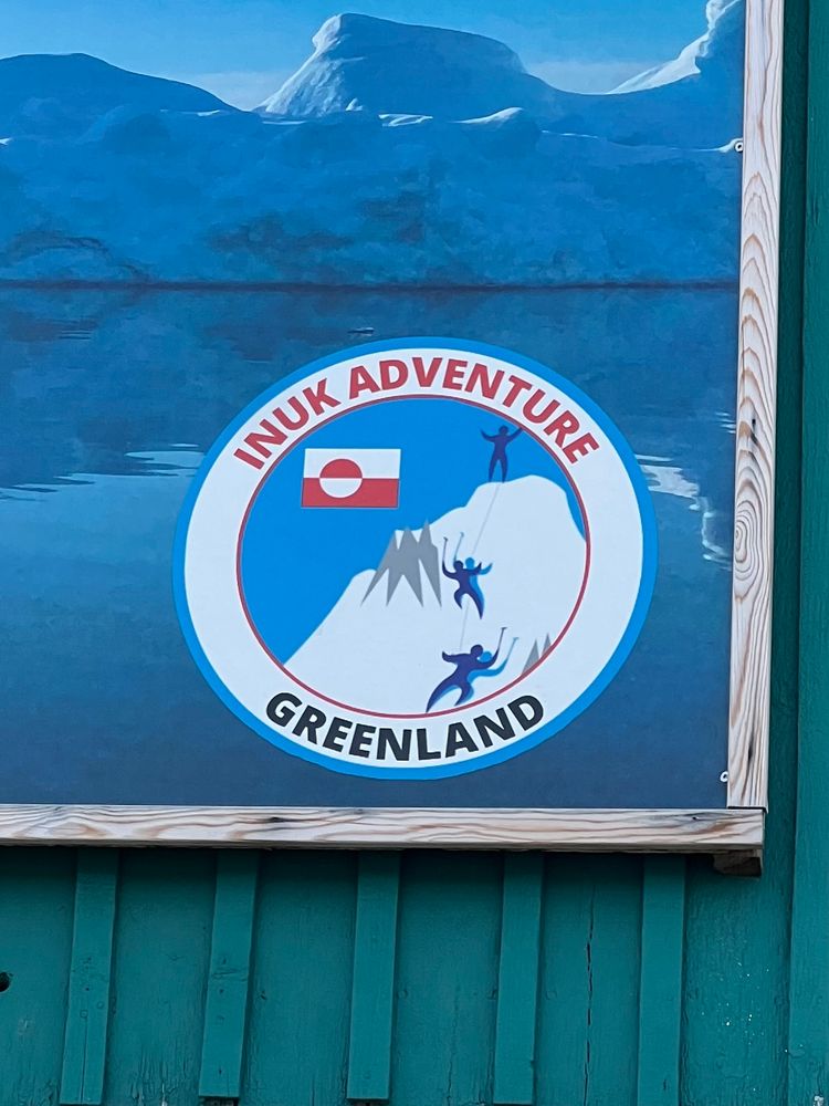 Logo for Inuk Adventure outfitter showing an iceberg, the Greenlandic flag, and three figures either in triumph or extreme peril, unclear