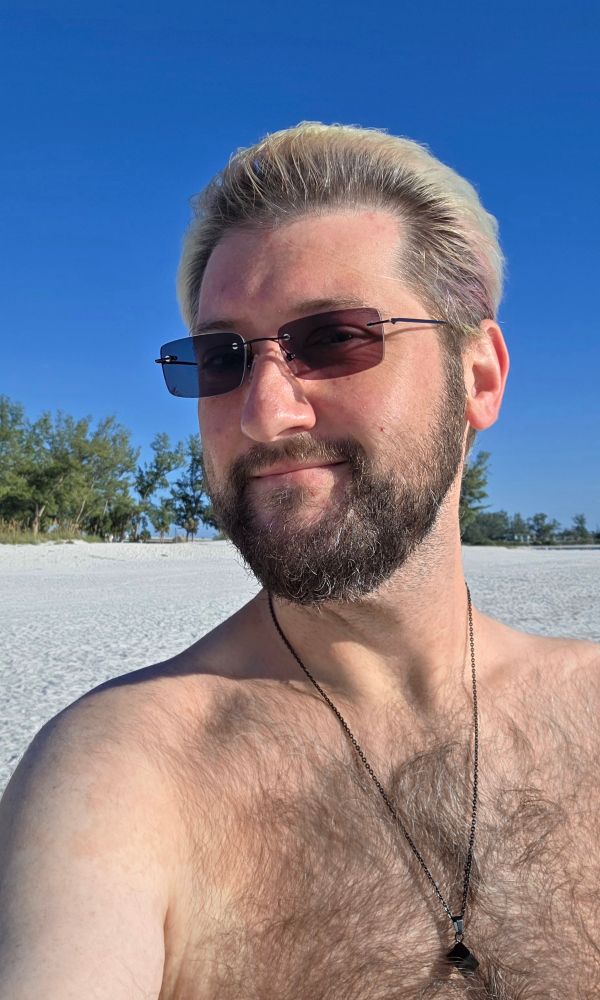 Me shirtless at the beach with sunglasses and a smile. Hair is slicked back by the wind.