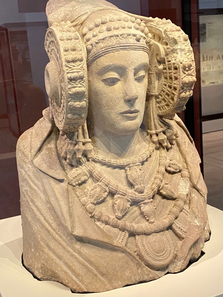 A limestones bust representing a lady, richly attired and wearing a headdress composed of a tiara covered by a veil, a diadem on the forehead and, on the sides, wheel-like coils (rodetes) that frame the face in which the hair would have been gathered.